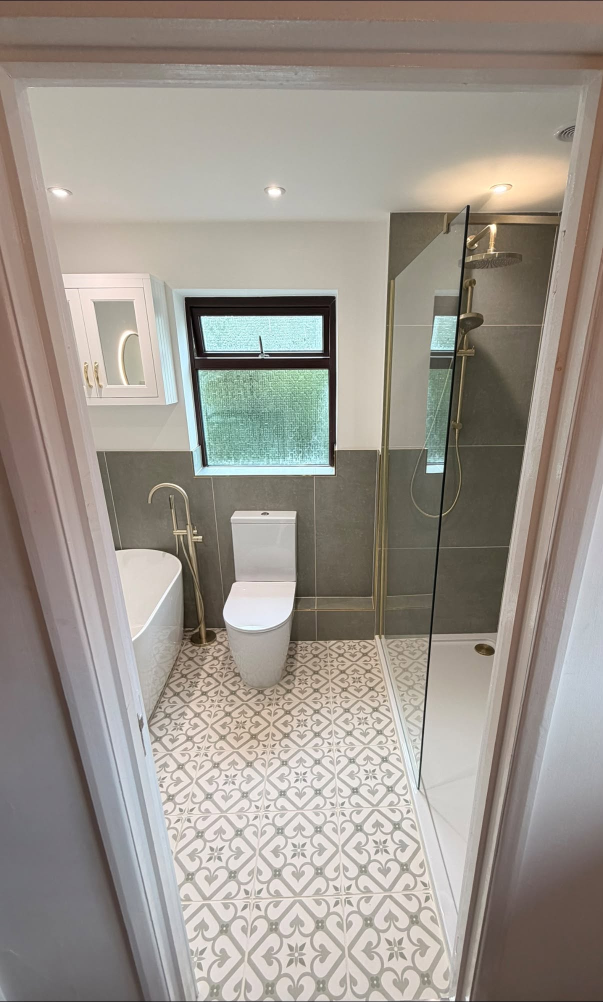 The same bathroom after: freestanding bath, patterned floor tiles, brass fittings and a walk-in shower