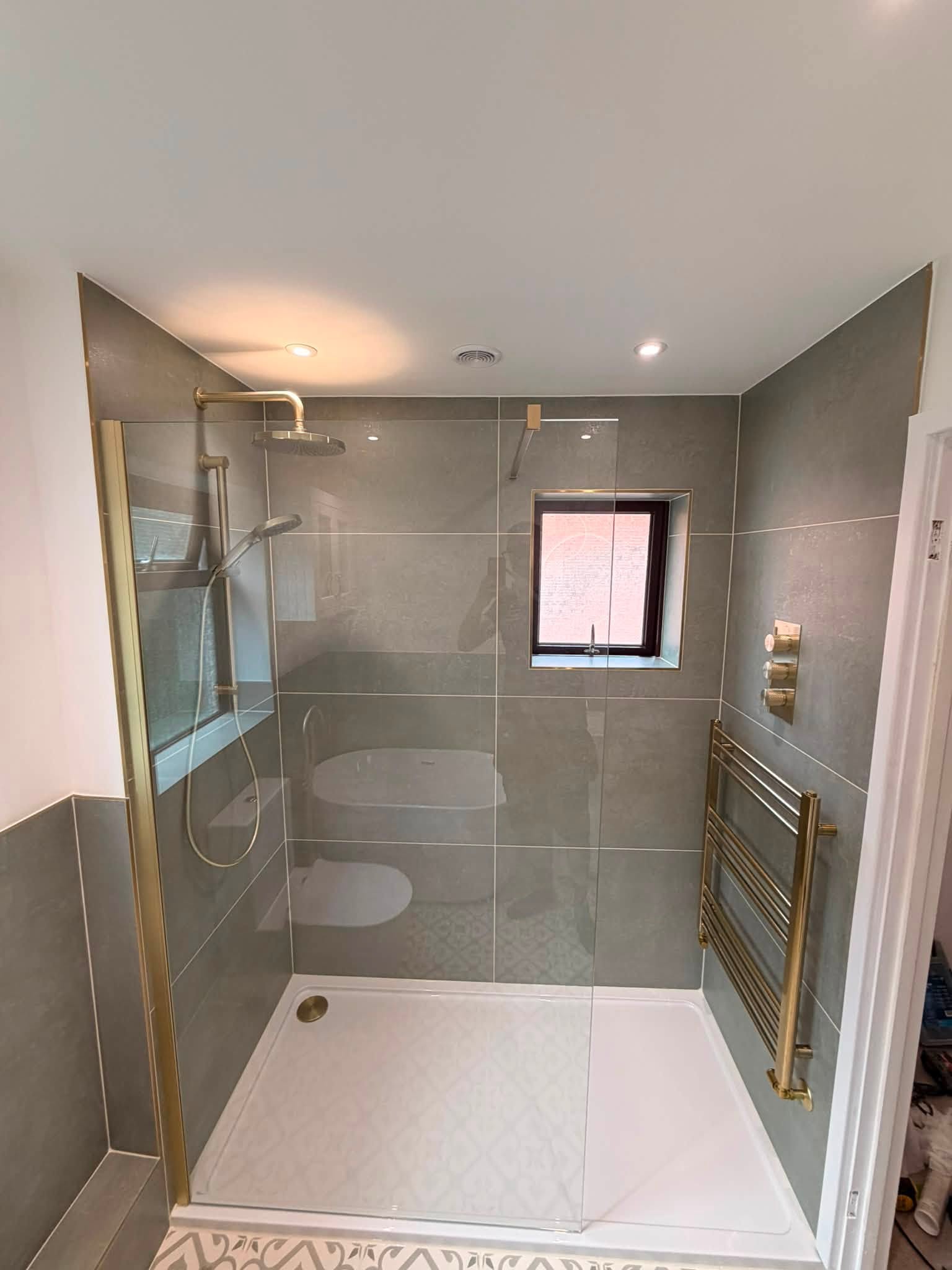 After: walk-in shower with brass fittings beside a brass towel rail