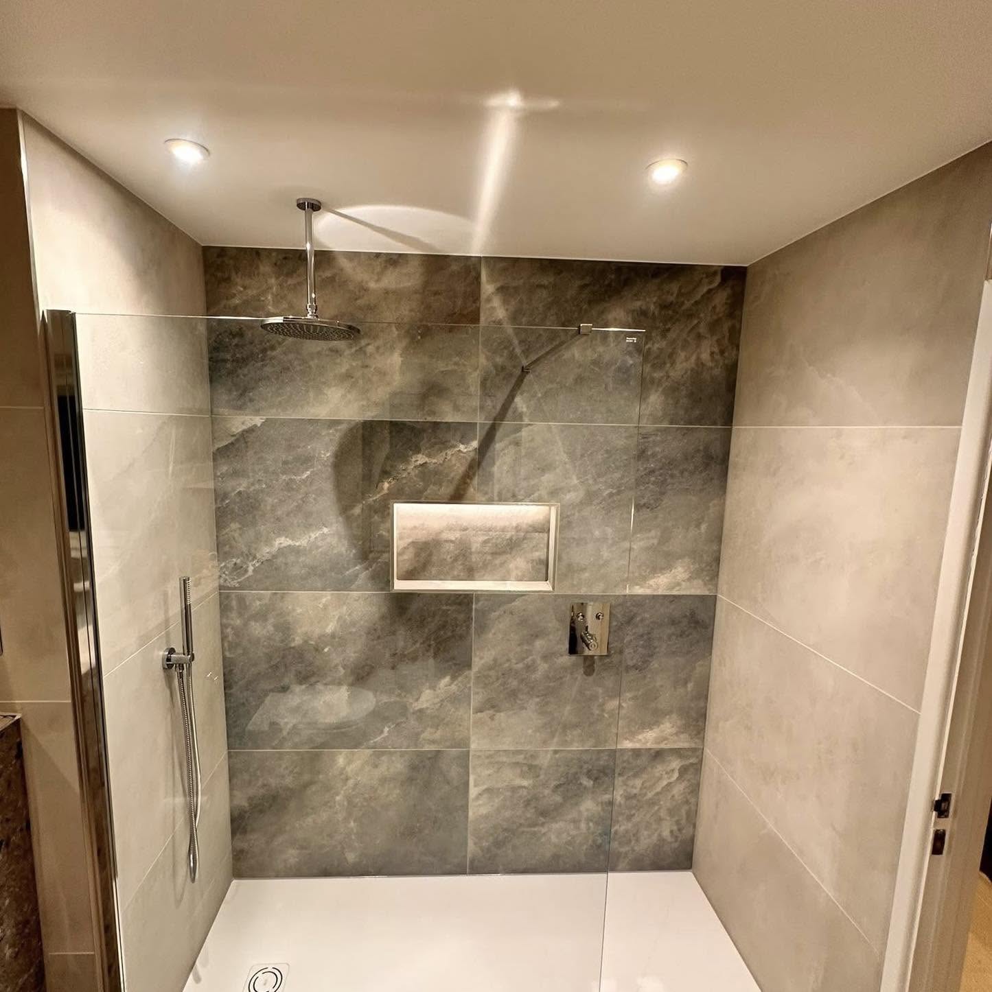 Walk-in shower with a dark marble-effect feature wall, lit niche and ceiling rain head