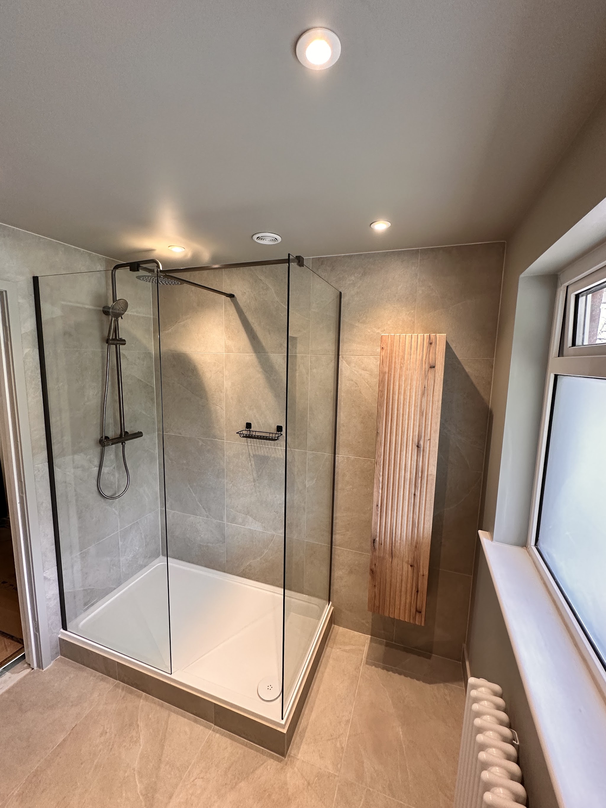 Walk-in shower enclosure with matt black fittings and a slatted timber cabinet