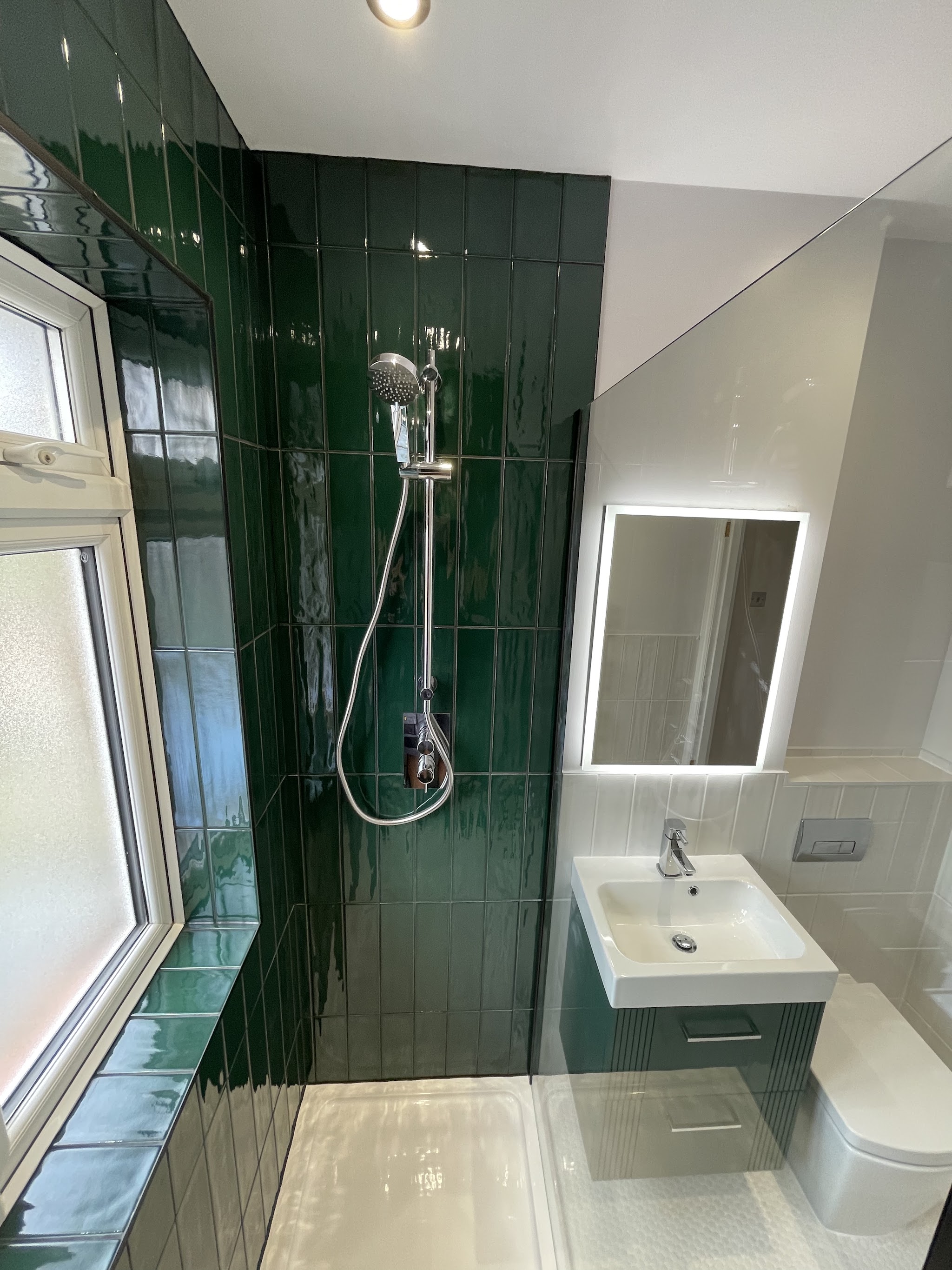 Deep green gloss tiled shower wall with an LED mirror and wall-hung basin