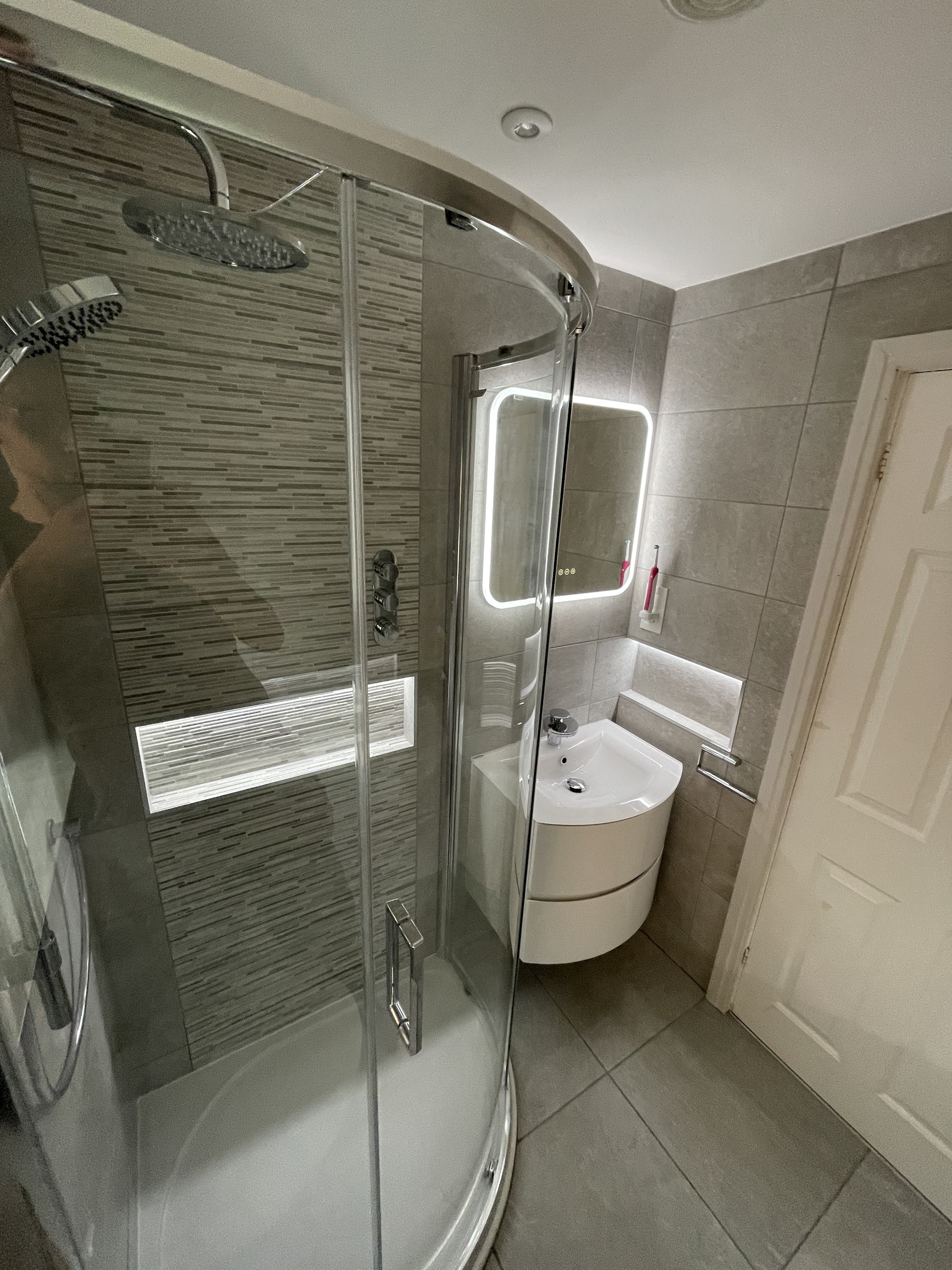 Quadrant shower with a lit mosaic niche, curved vanity unit and LED mirror