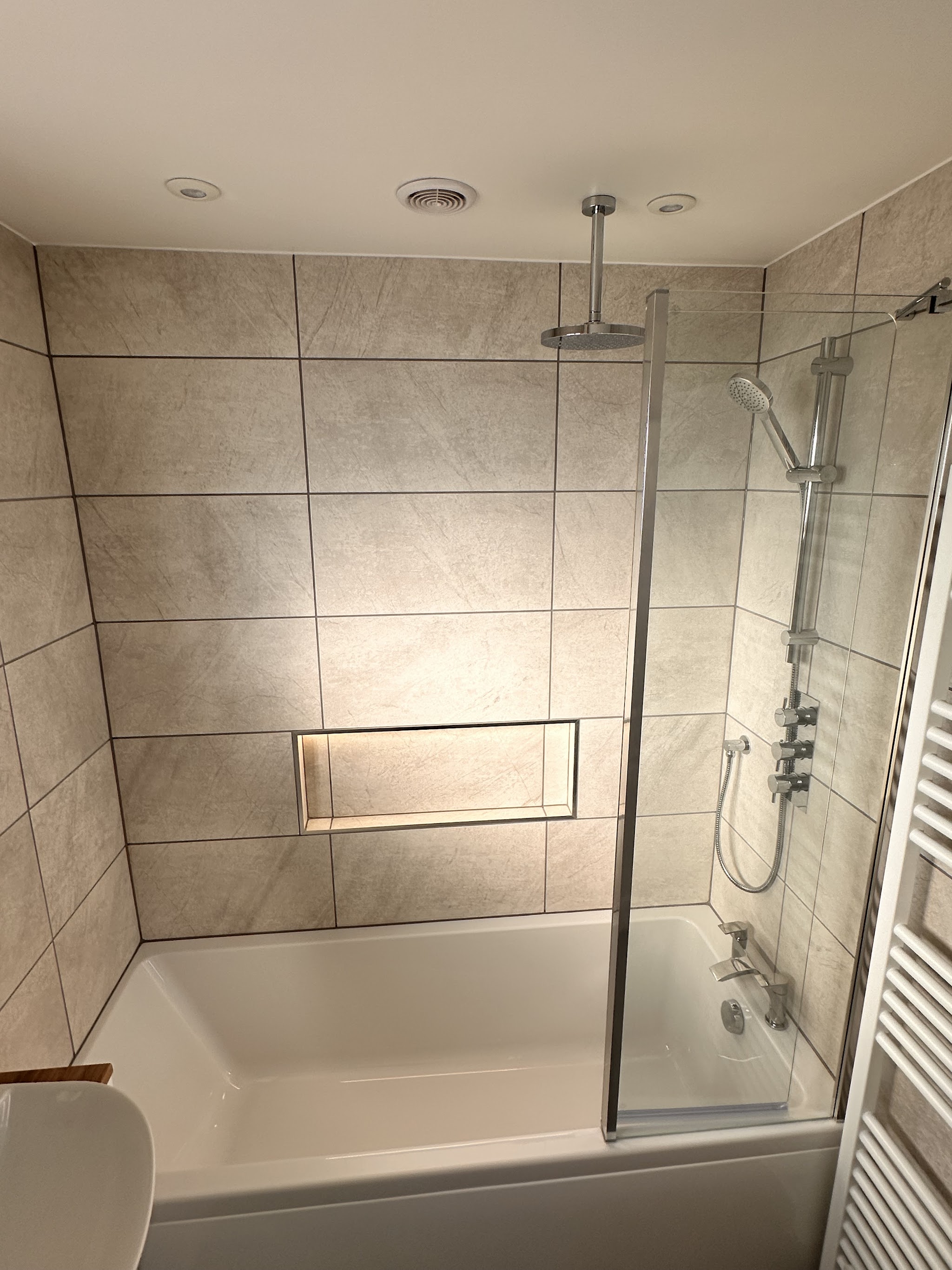 Shower over bath with large-format tiles, a lit recessed niche and ceiling rain head