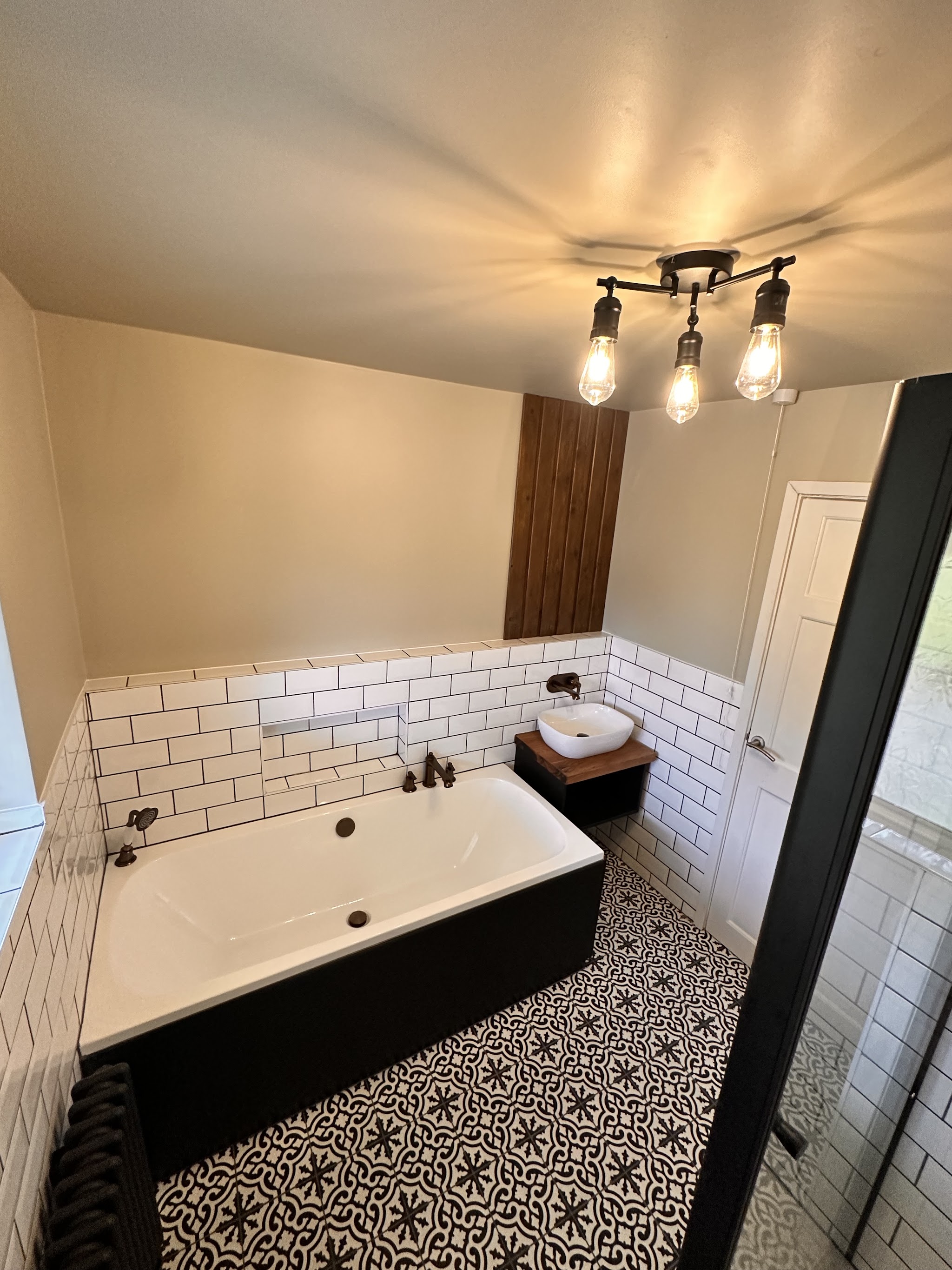 Bathroom with a black-panelled bath, white metro tiles, a patterned floor and filament pendant light