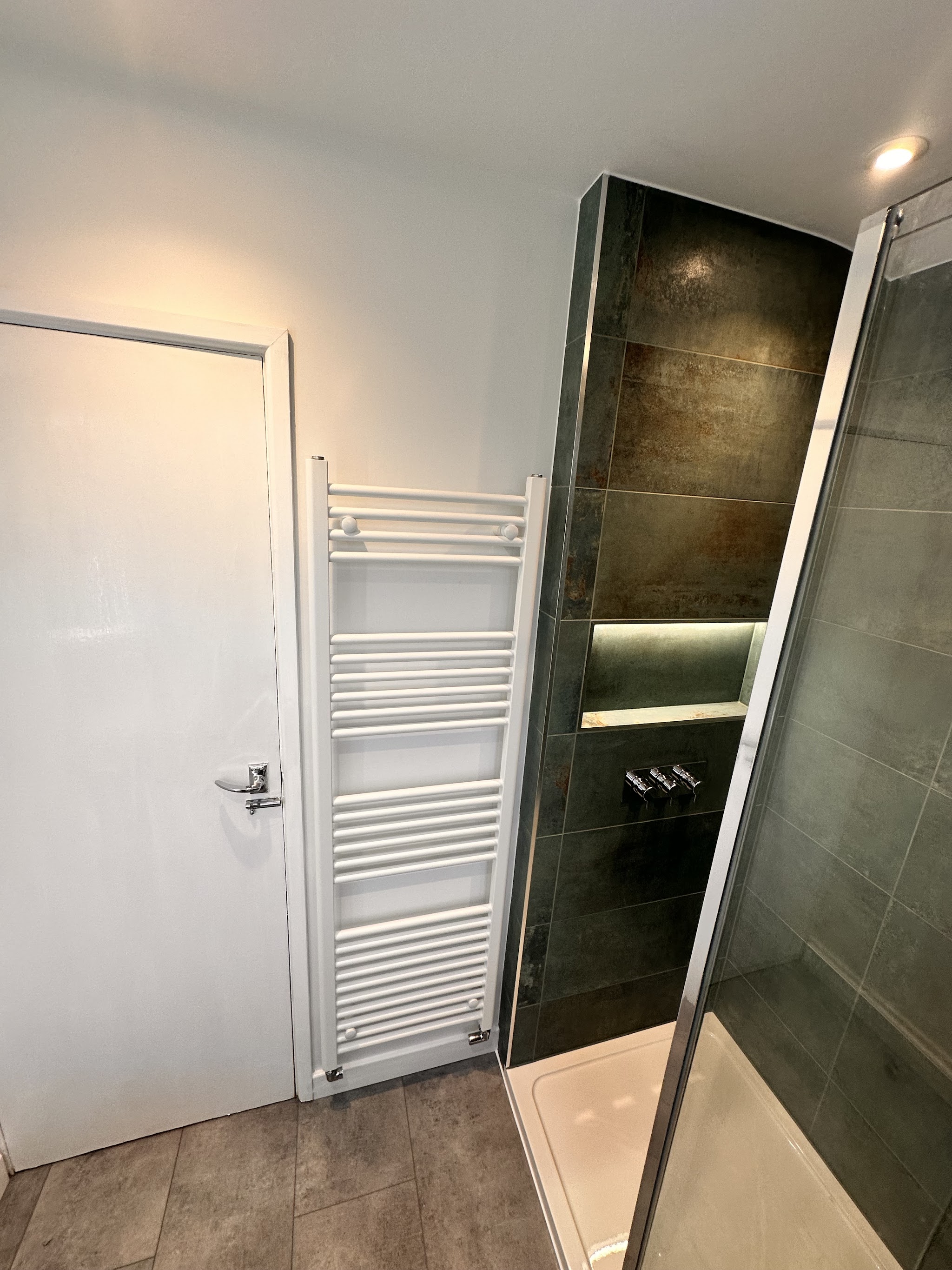 Dark tiled shower with a lit niche beside a white towel rail