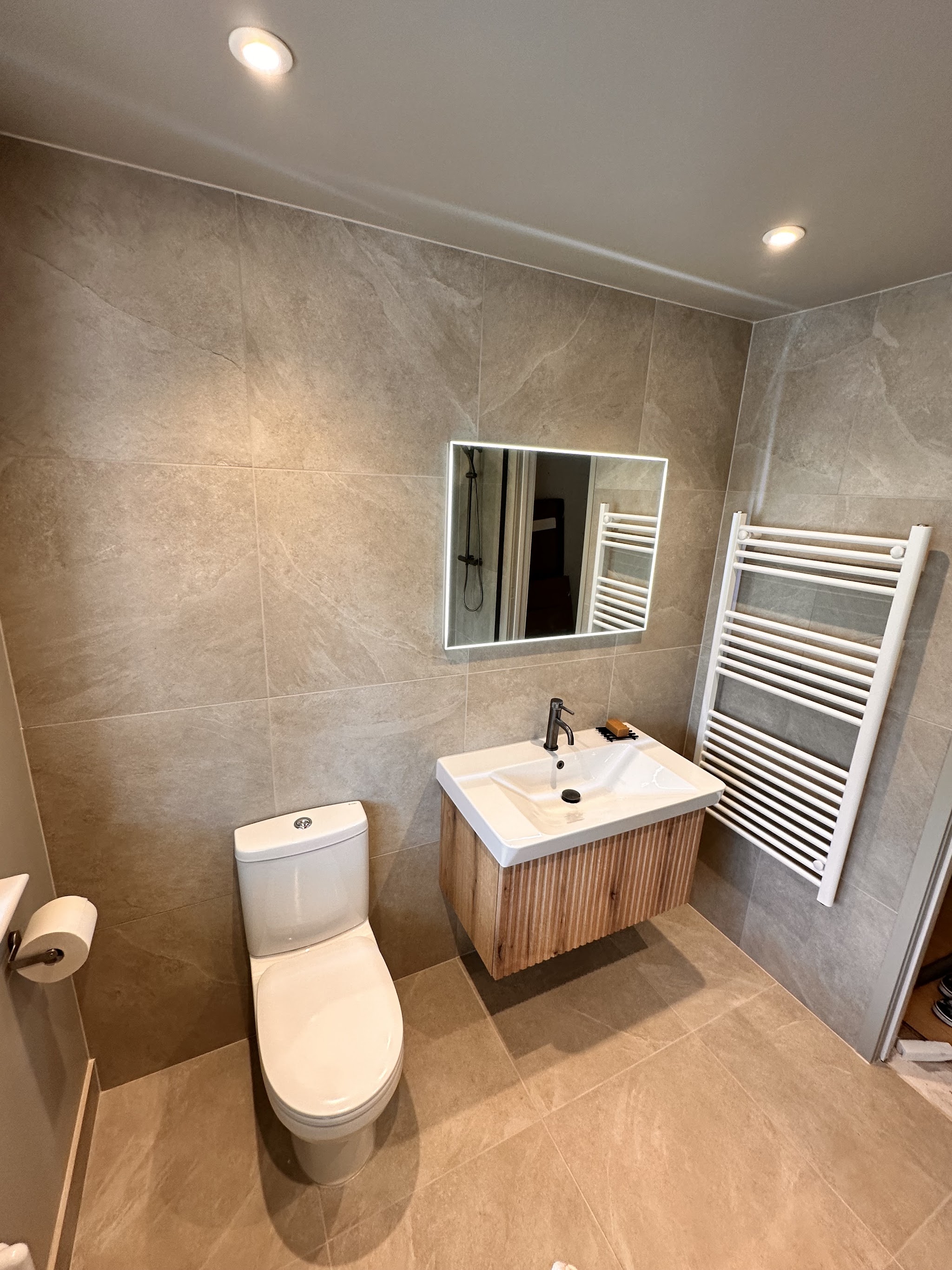 Fluted timber vanity, close-coupled WC and white towel rail on grey tiles